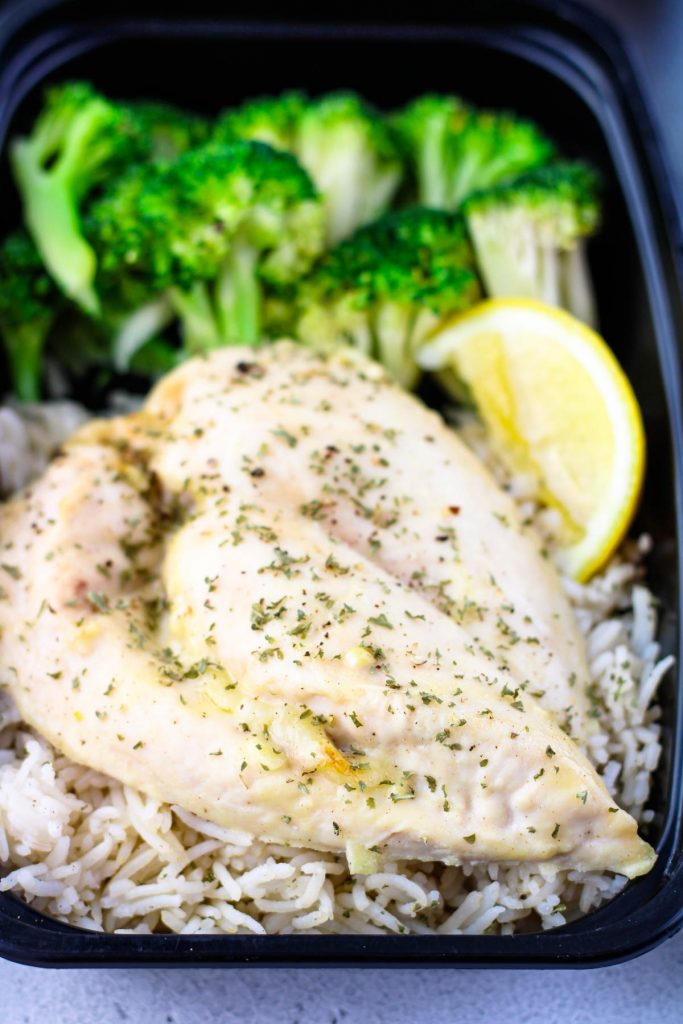 A chicken breast in a container with broccoli and rice.