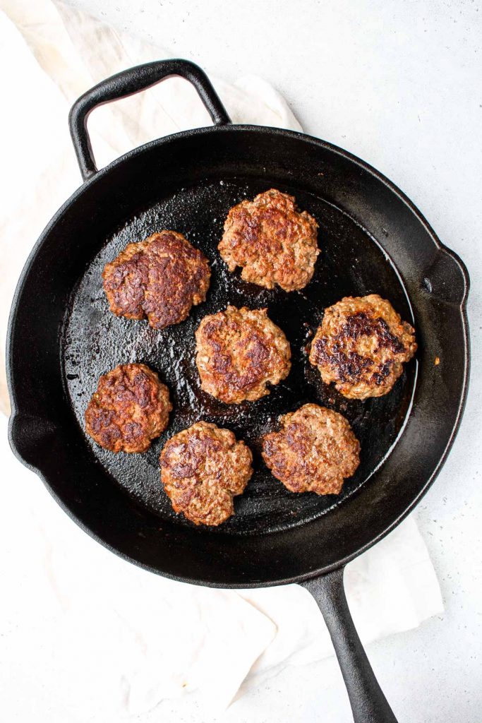 A large cast iron skillet with cooked burgers on it.