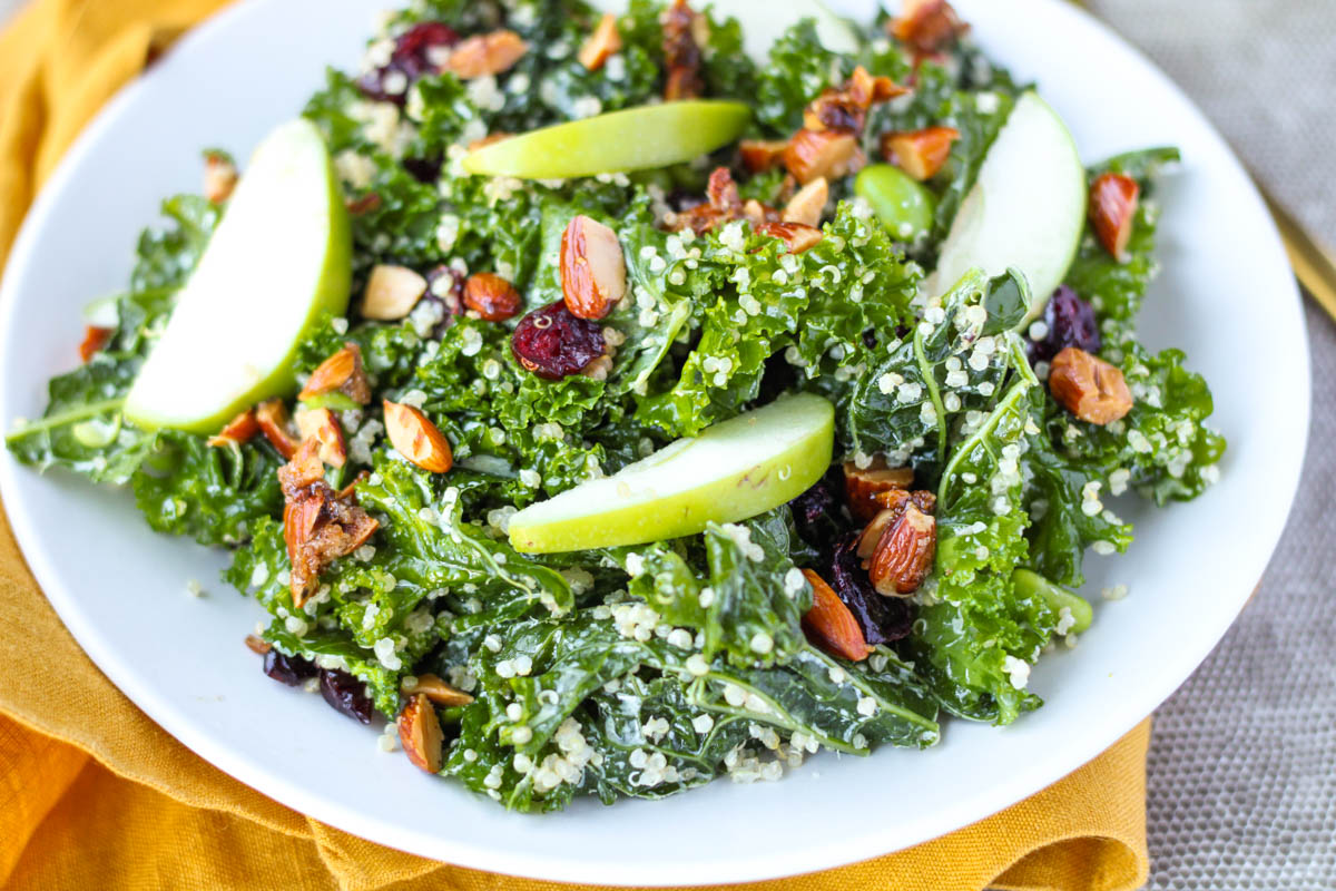 Kale salad with nuts and apple on a white plate.