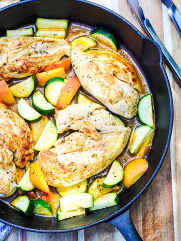 One Pan Chicken Breast with Zucchini and Peaches in a castiron skillet on a brown cutting board