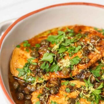 A white skillet with cooked chicken and capers.