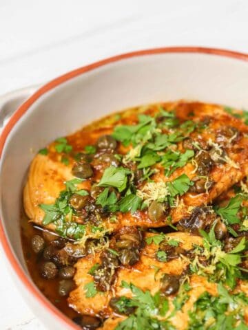 A white skillet with cooked chicken and capers.