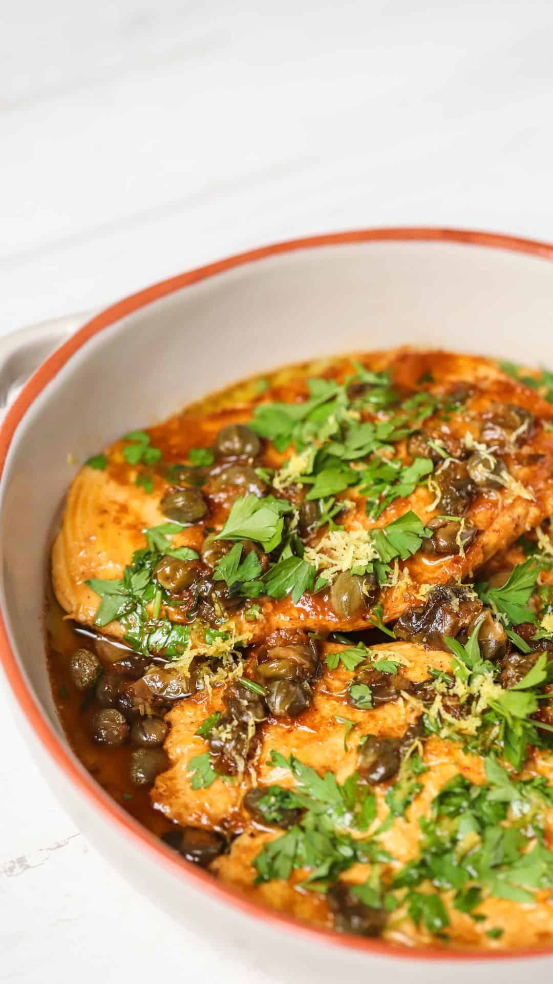 A white skillet with cooked chicken and capers.
