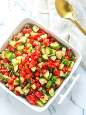 Overhead shot of Strawberry Cucumber Salad with Mint in a white serving dish on a white marble countertop