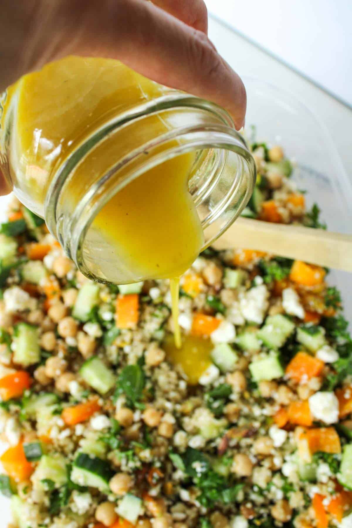 Pouring dressing overtop healthy quinoa salad ingredients.