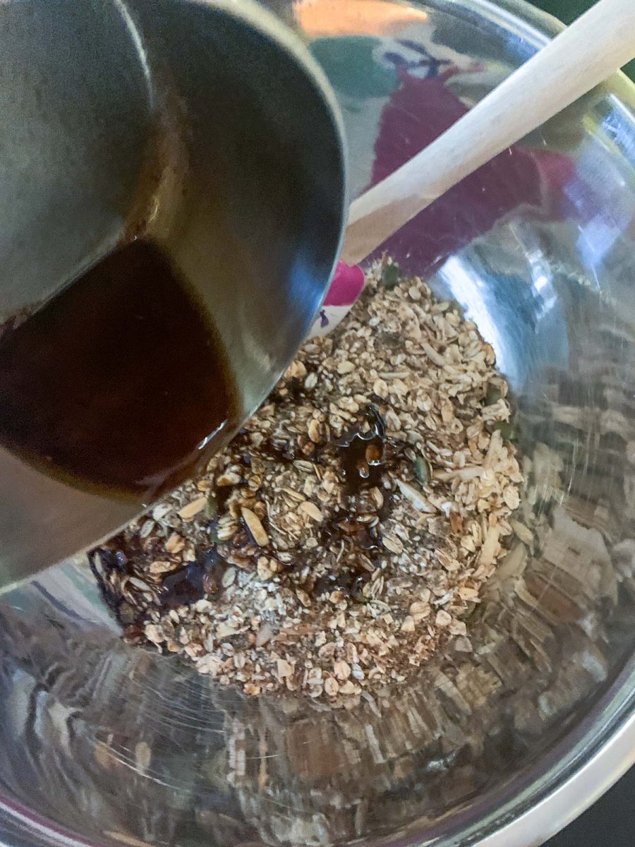Pouring a saucepan of maple syrup and oil with cinnamon over the healthy granola in a bowl