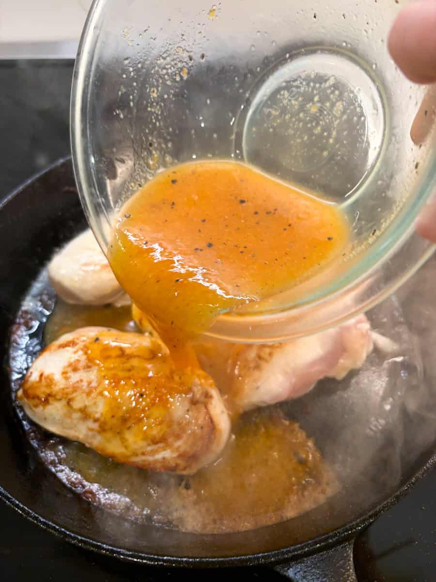 Pouring peach sauce over cast iron chicken breasts.