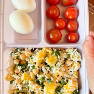 Meal prep container with rice salad, hard boiled eggs and cherry tomatoes.