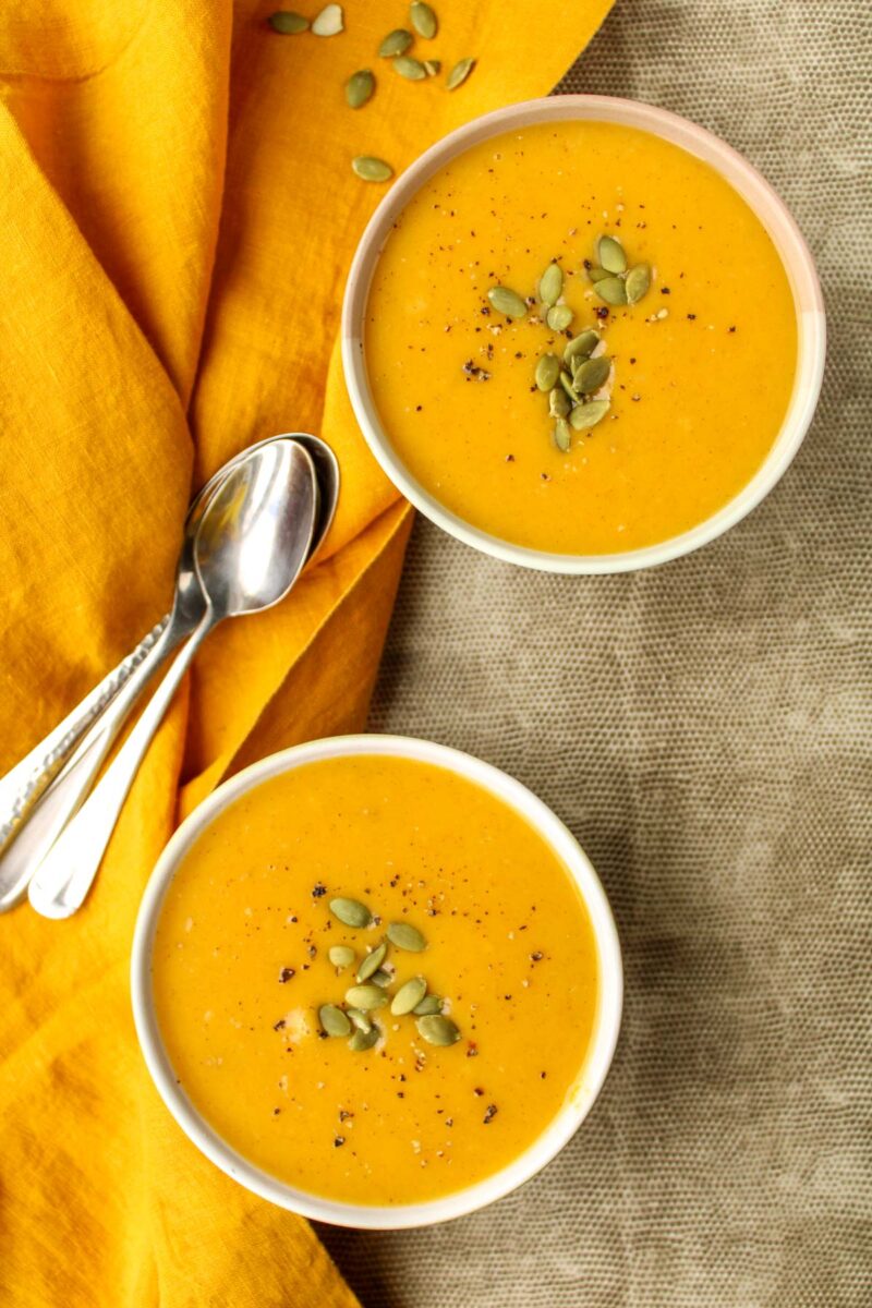 Two bowls of butternut squash soup on a grey placemat.