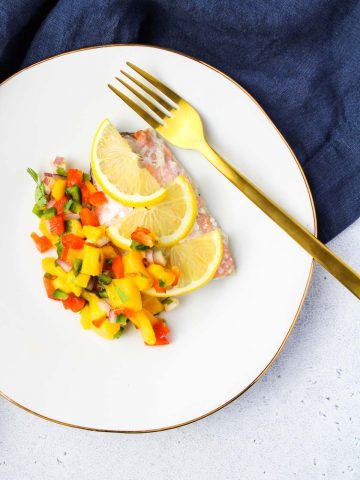 Mango salsa and salmon with lemon slices on a plate with a gold fork.