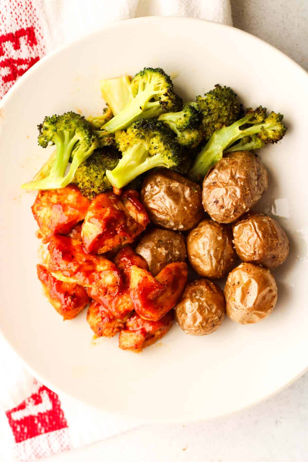 A while plate with BBQ chicken breast chunks, broccoli and roasted potatoes.