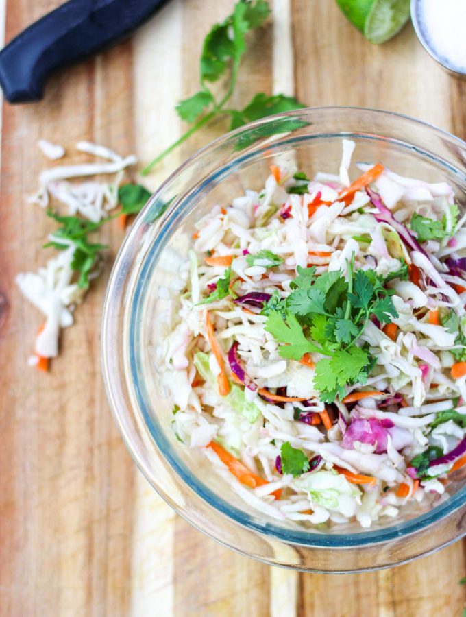 A clear bowl of coleslaw on a cutting board