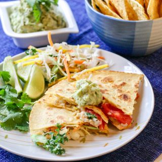 Simple Haddock Quesadillas on a blue placemat and a white plate with a bowl of tortiall chips in the background