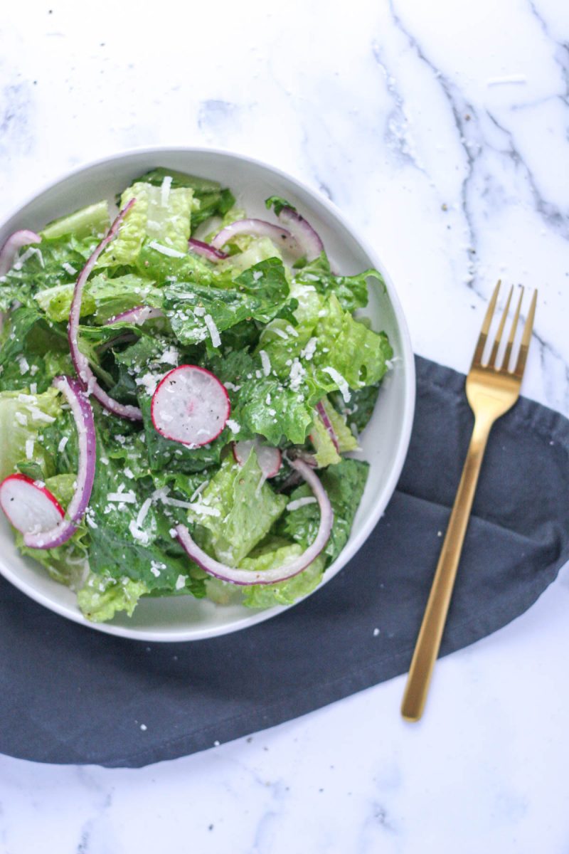 Simple Romaine Salad with Radish and Parmesan on a white plate with a gold fork