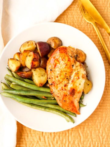 Slow cooked chicken on a white plate with potatoes and green beans.