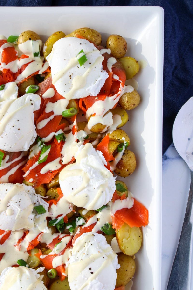 A white platter filled with roasted potatoes, smoked salmon and boiled eggs.