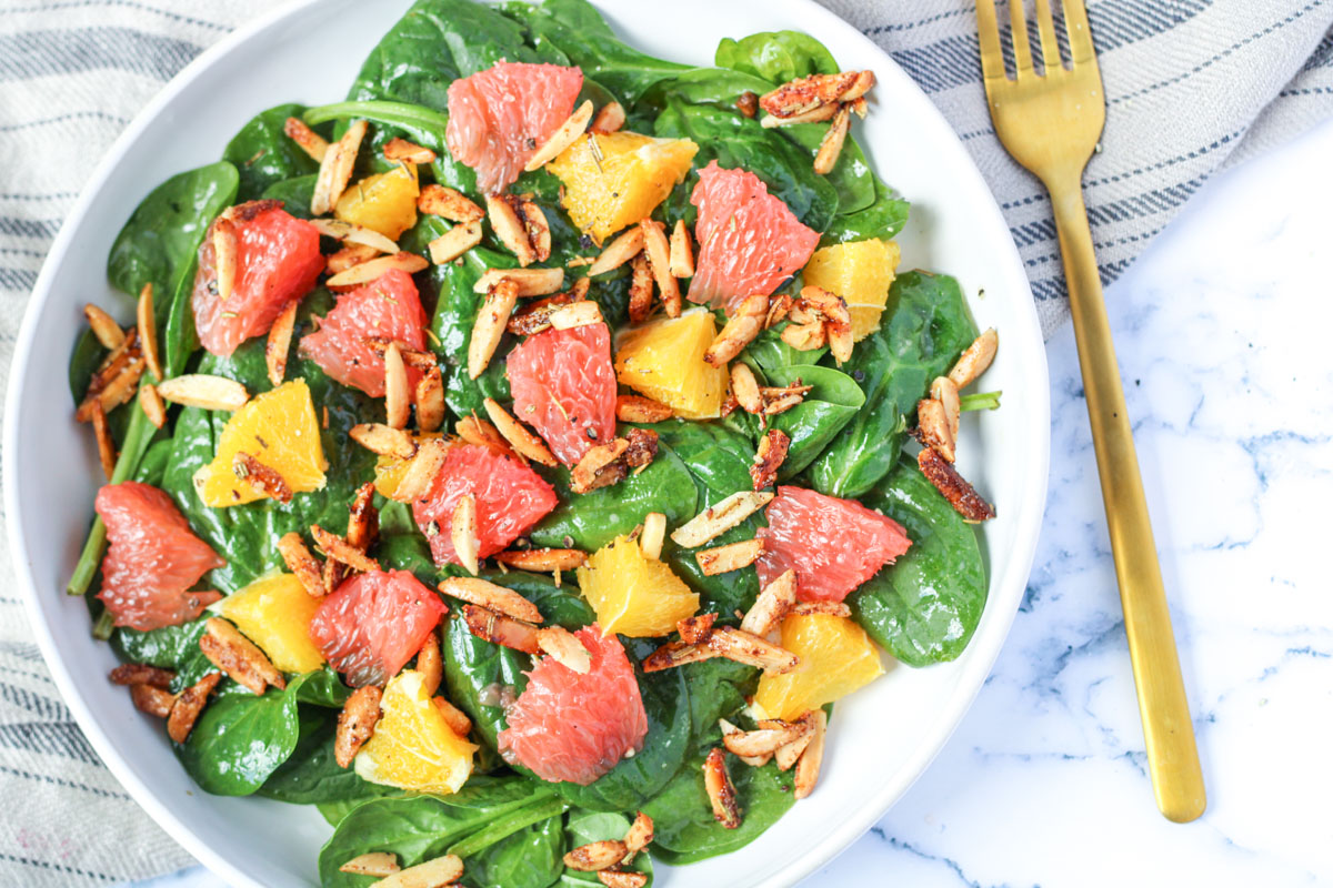 a white plate filled with spinach and citrus salad and nuts