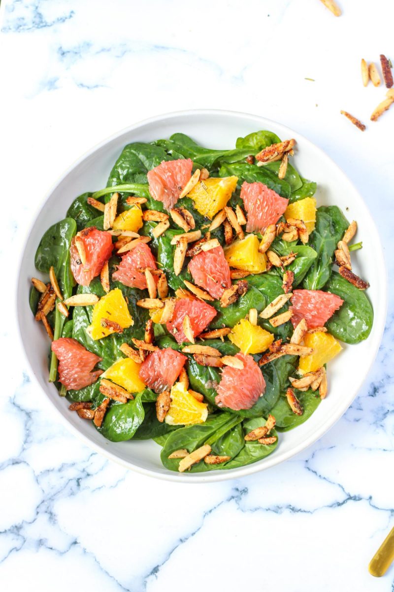 A round white plate filled with a spinach and grapefruit salad.