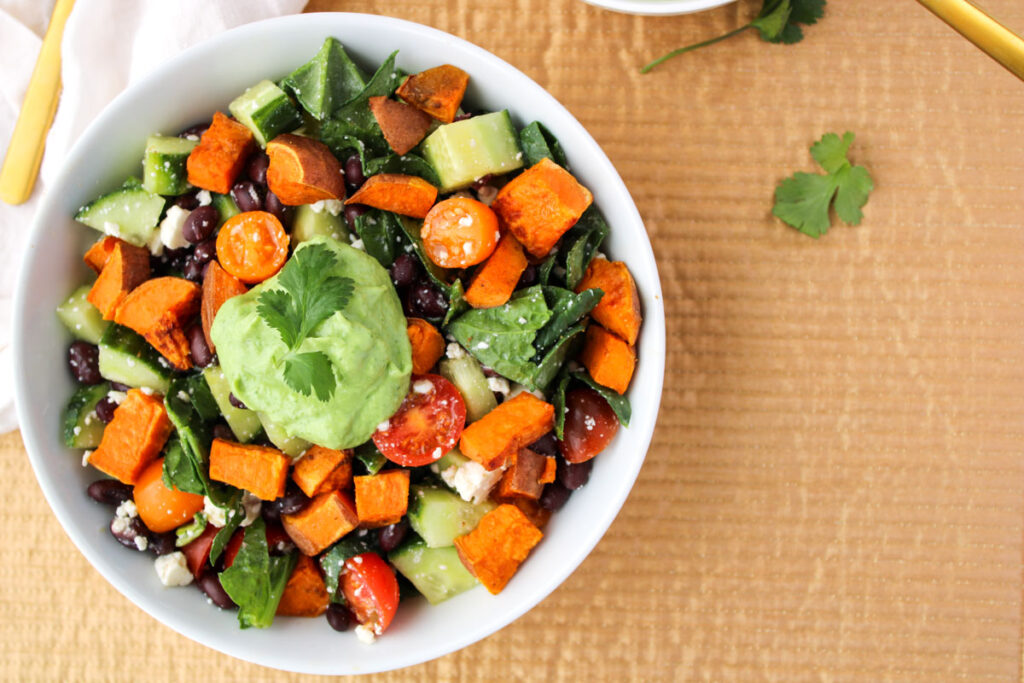 Salad with roasted sweet potatoes, spinach and feta in a white bowl.