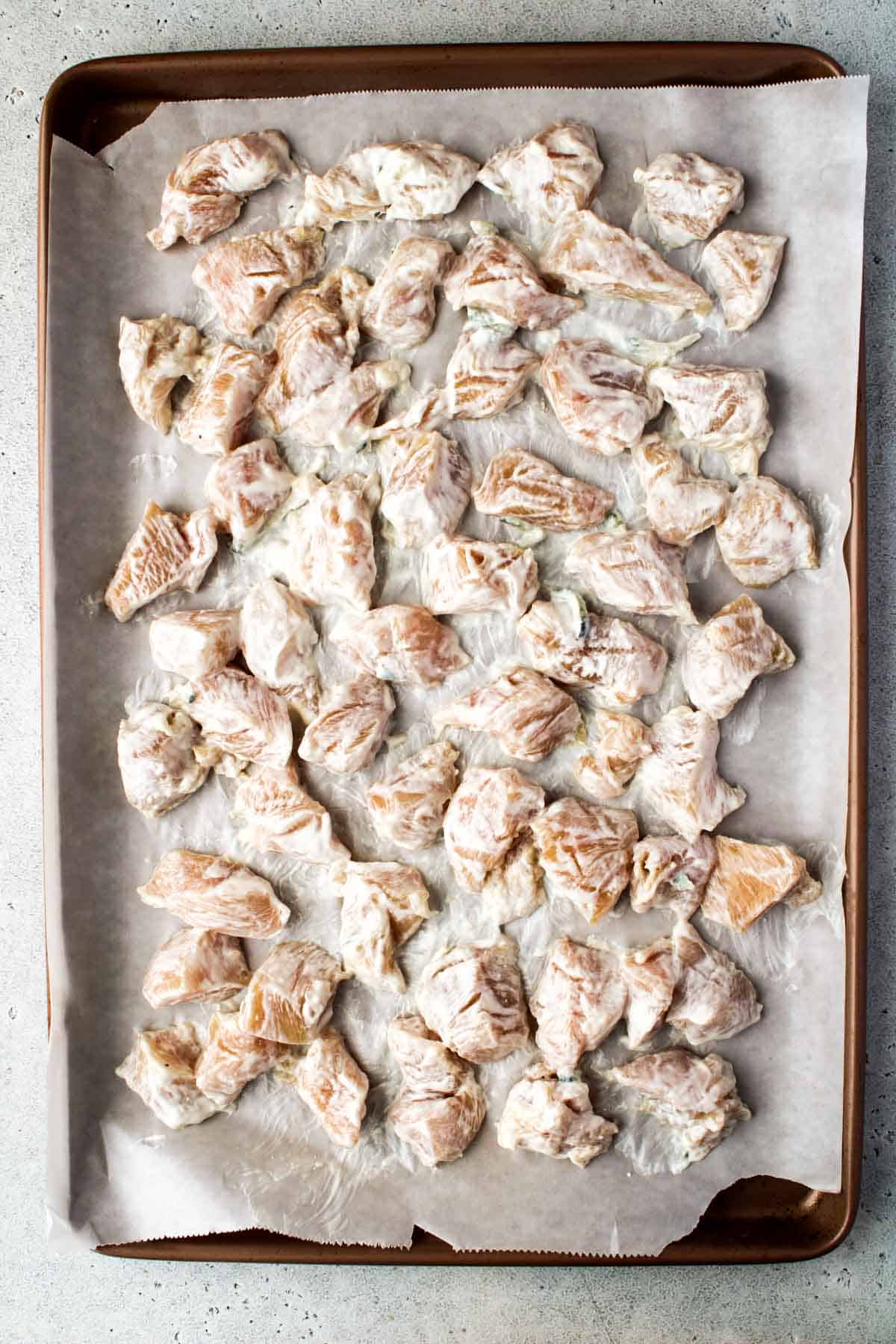 Chicken breast cubes on a prepared pan.