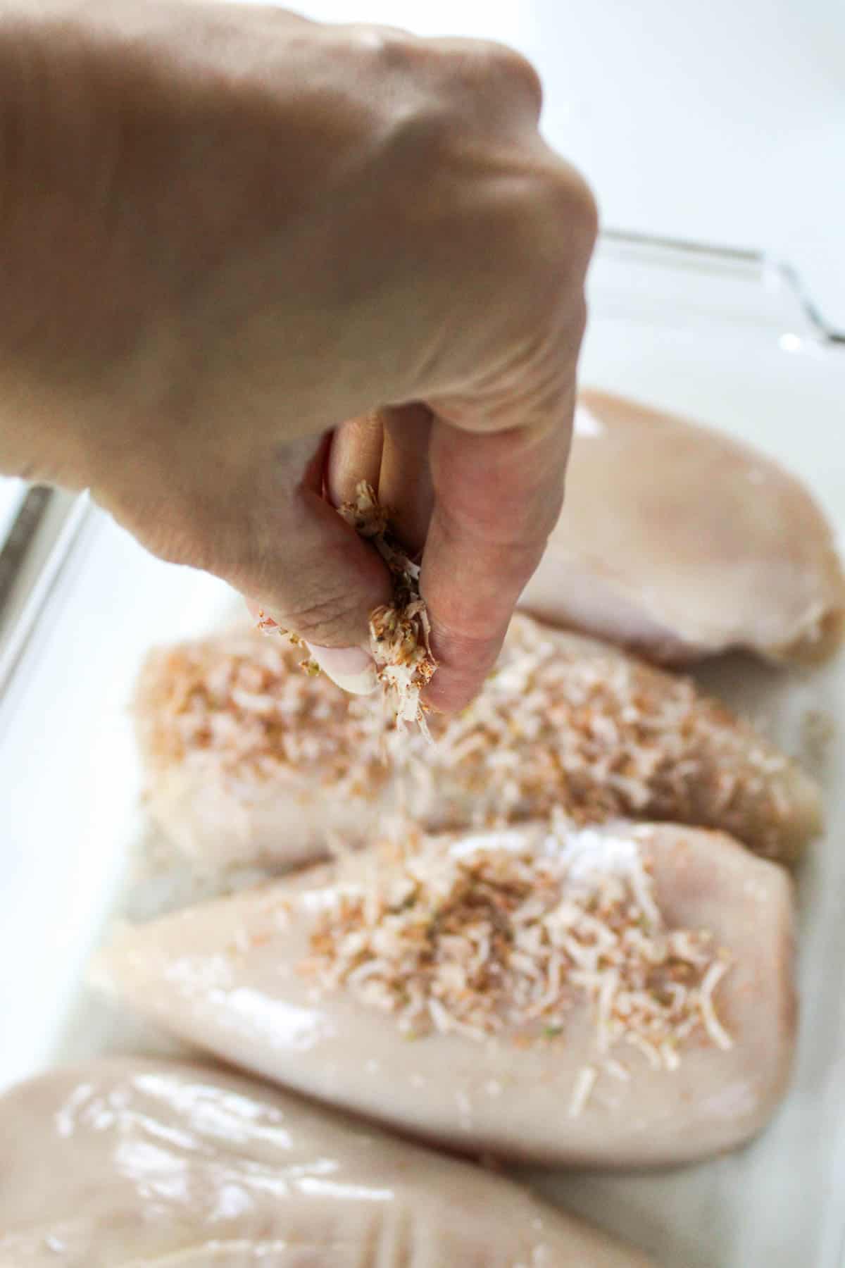 Sprinkling cheese and herb mixture overtop chicken breasts.