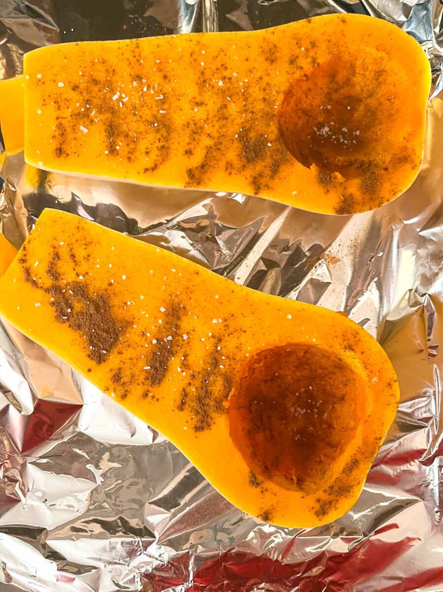 Butternut squash halves with cinnamon and salt on a tinfoil covered pan.