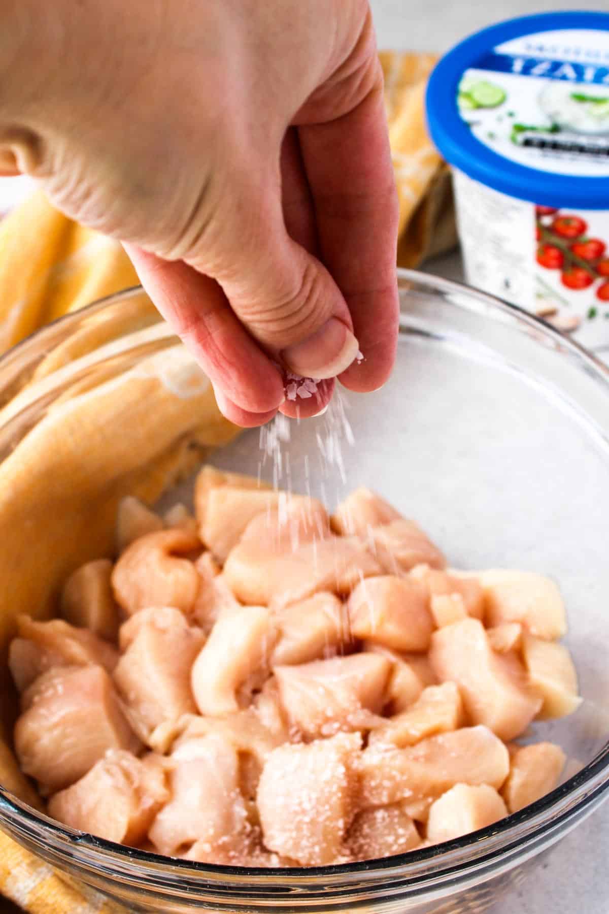 Sprinkling chicken breast cubes with Kosher salt.