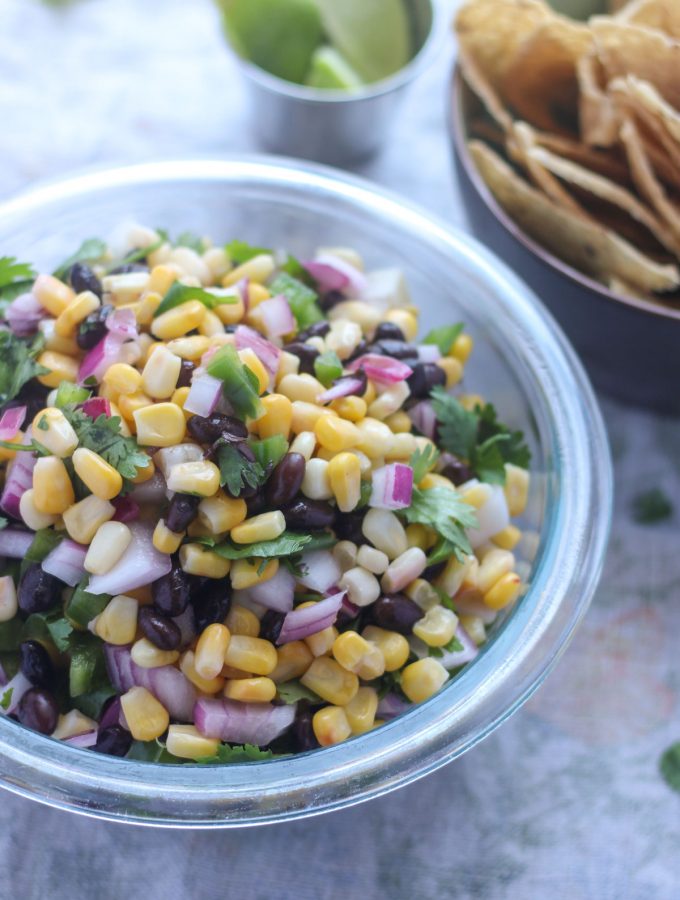 A bowl of corn salsa with a small bowl of chips beside it.
