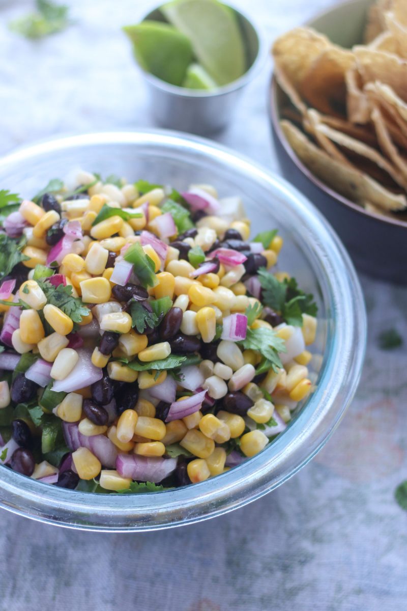 A bowl of corn salsa with a small bowl of chips beside it.