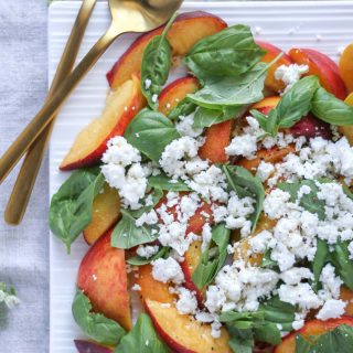 Summer Peach Basil Salad with Feta on a white platter with gold flat wear