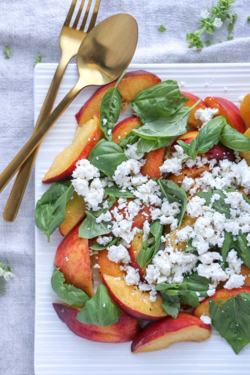 Summer Peach Basil Salad with Feta on a white platter with gold flat wear