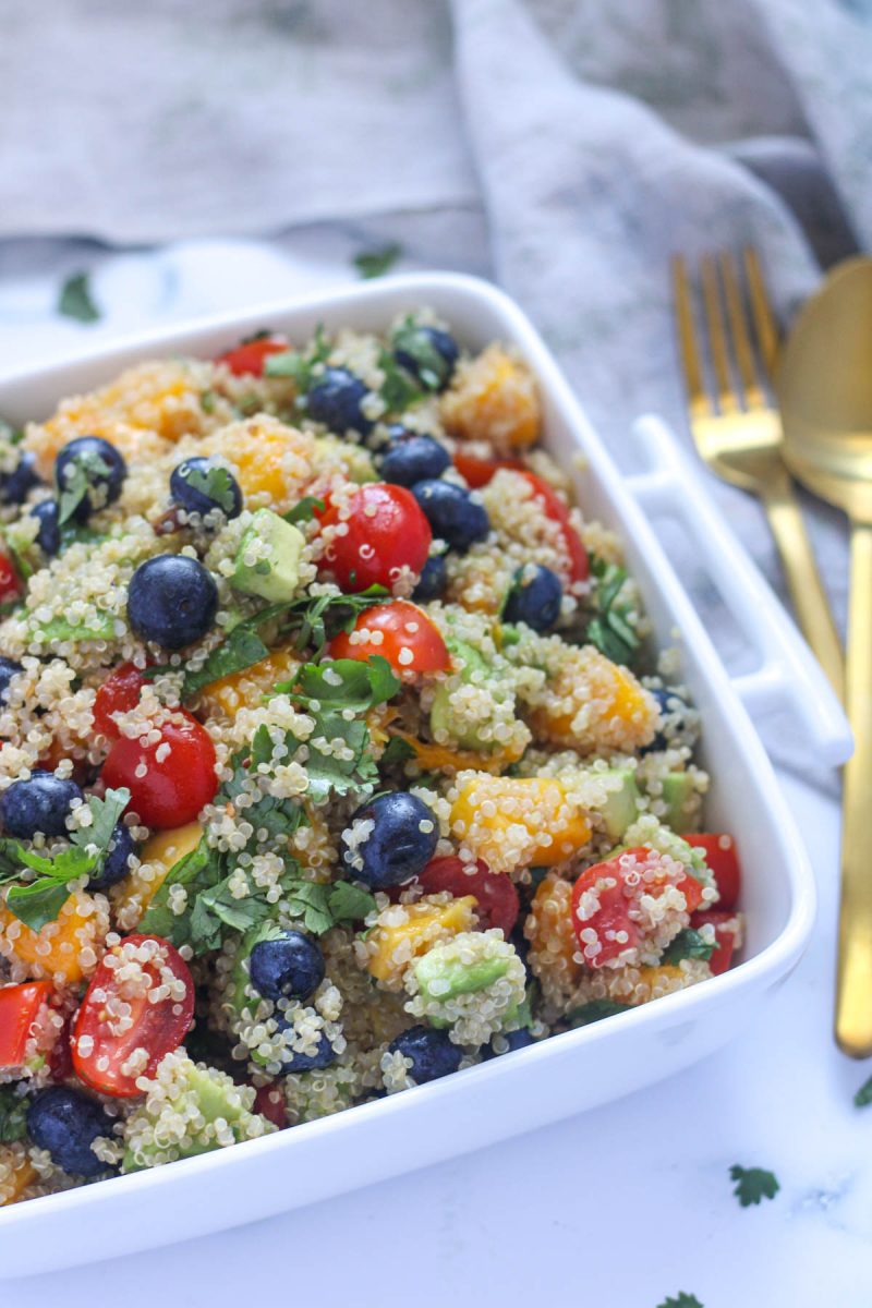 Summer Quinoa Salad with Mango and Blueberries in a square white dish with a gold fork and spoon beside it