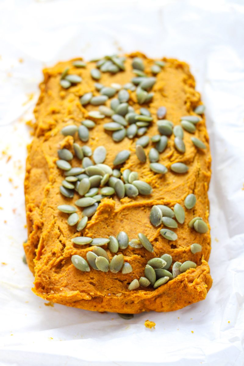 A loaf of pumpkin bread top with pepitas on parchment paper