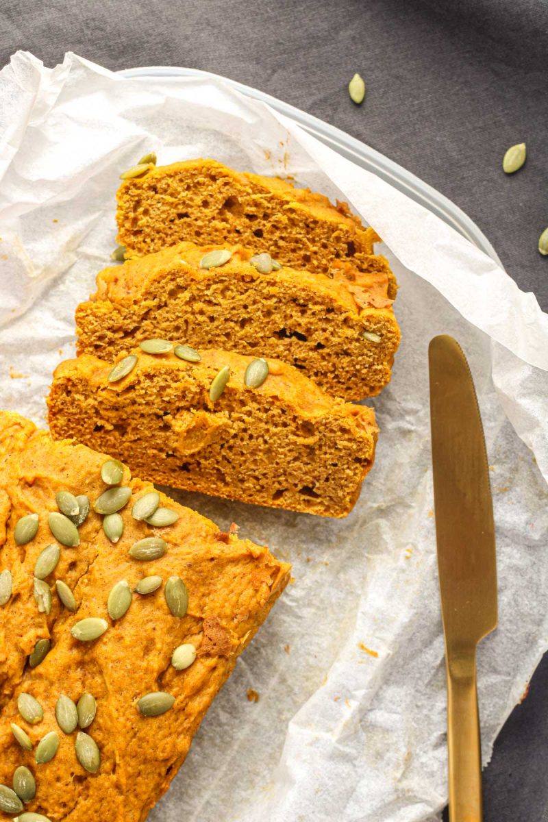 Three slices of pumpkin loaf on parchment paper with a gold knife beside them