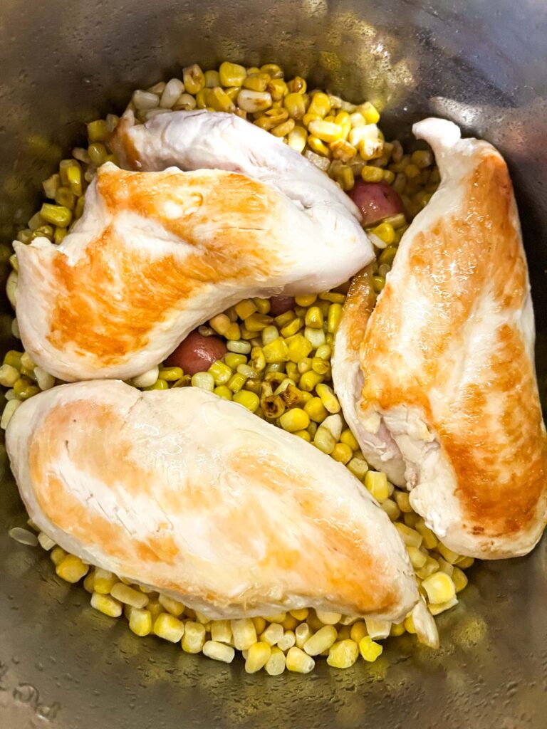 Chicken breasts on top of corn and potatoes.