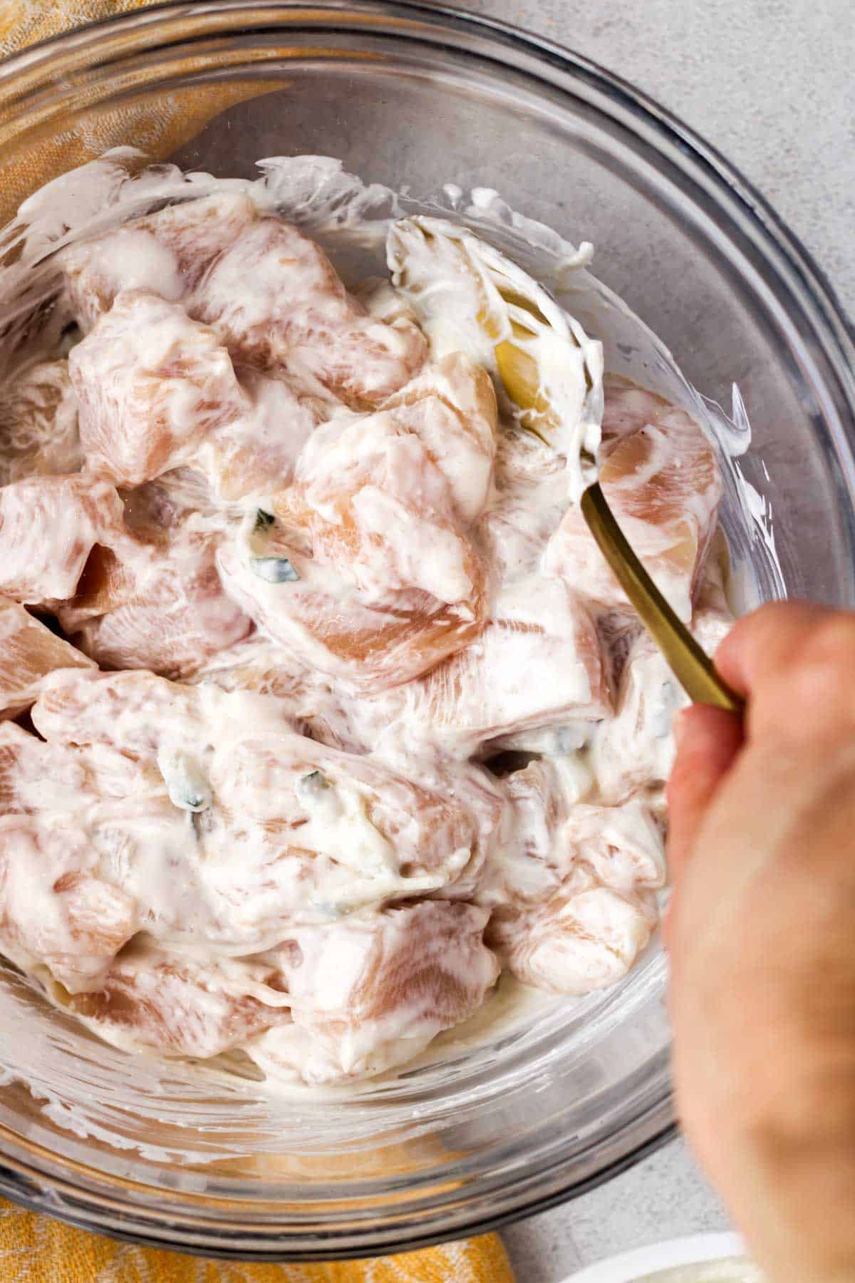 Chicken breast bites in tzatziki in a glass bowl.