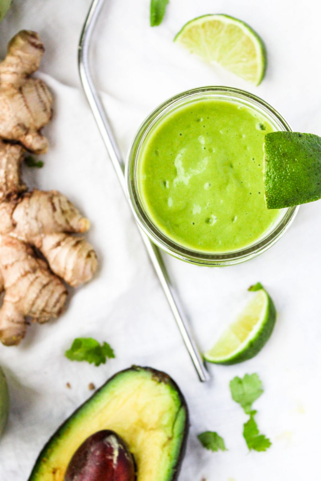 Tropical Green Smoothie with ginger root and avocado beside it