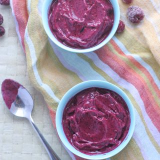 Two bowls of Healthy 5 Ingredient Berry Frozen Yogurt on a colourful tea towel with a spoon and frozen raspberries on the side