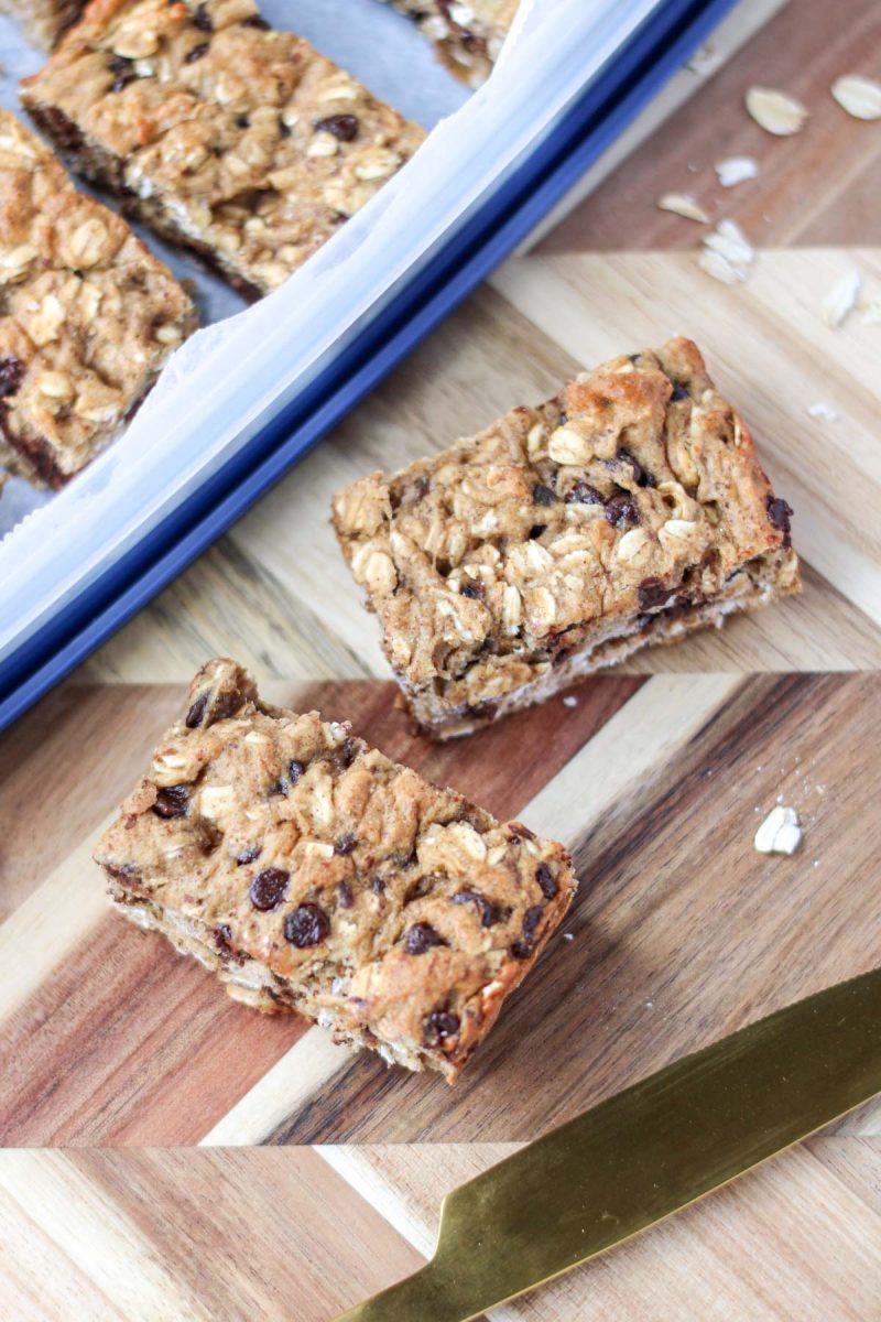 Two square of gluten-Free Oatmeal Breakfast Bars with Chocolate on a wood cutting board.