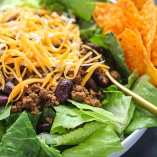 White plate with romaine lettuce ground beef and shredded cheese with nacho chips