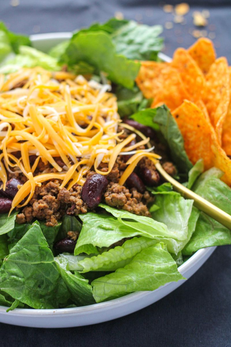 White plate with romaine lettuce ground beef and shredded cheese with nacho chips