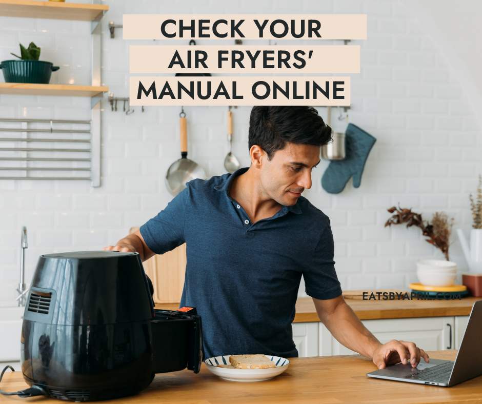 Man with air fryer and laptop in kitchen.